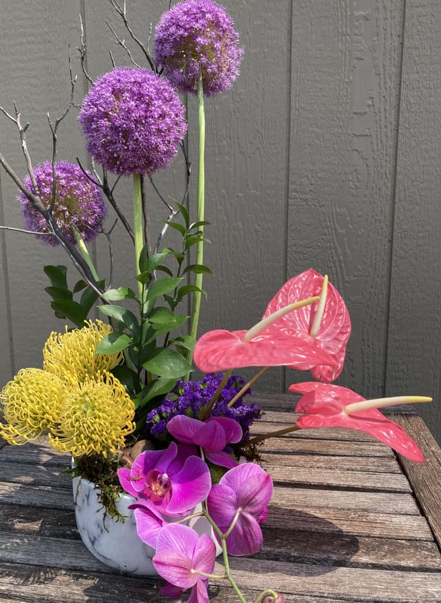 High-style arrangement of purple allium, pink anthurium, pincushion protea, and orchids