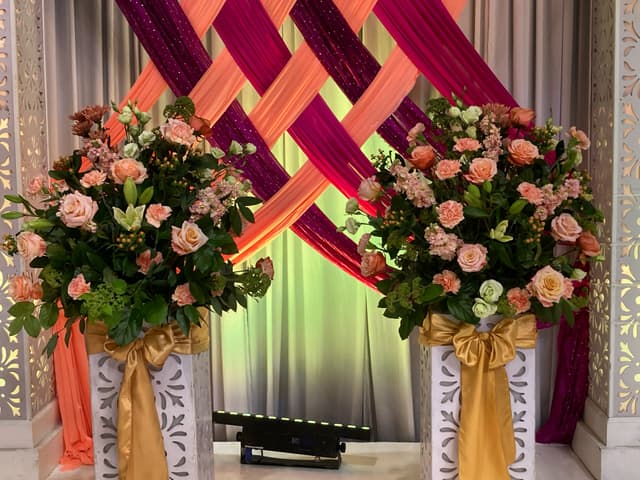 Large peach and coral floral displays on gold pedestals with draped fabric at an event