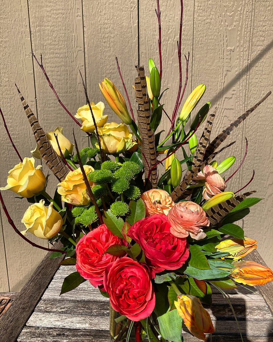 Red and yellow roses with green hydrangea and pheasant feathers, designed by Willow Creek Florist