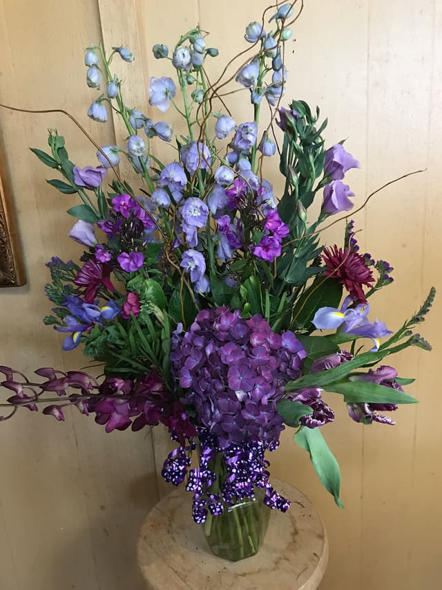 Tall all-purple arrangement of hydrangea, delphinium, and orchids
