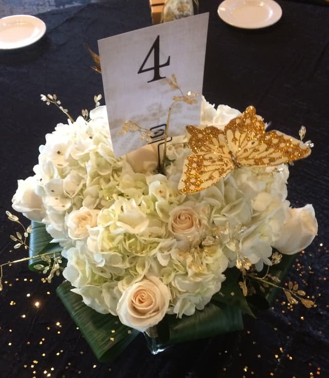 White hydrangea and rose centerpiece with a gold glitter butterfly and table number