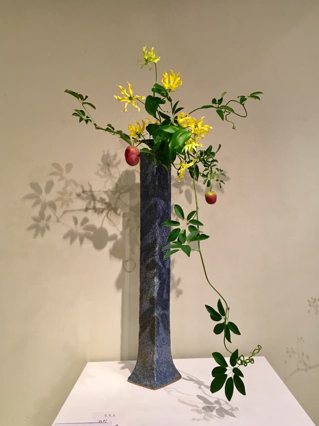 Tall Saga Go-ryū ikebana in a slender blue vase with yellow flowers