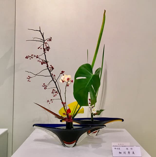 Ikenobō ikebana with an orchid, monstera leaf, and berry branches in a boat-shaped container