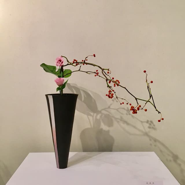 Ikenobō ikebana with pink blossoms and a red-berry branch in a tall black vase