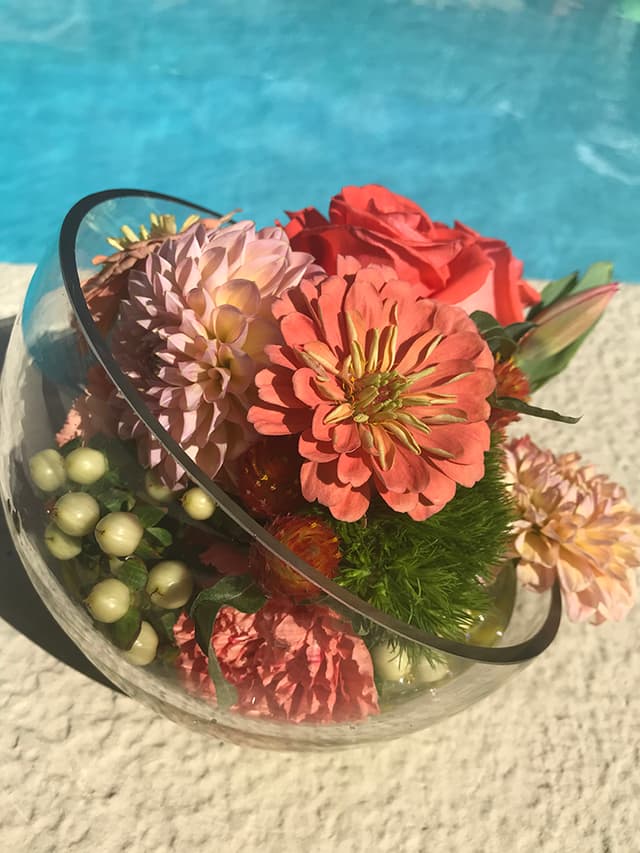 Coral roses and dahlias arranged in a glass bowl with greenery