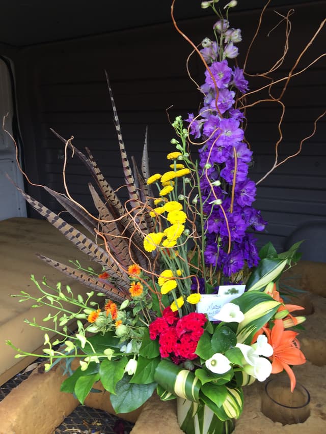 Dramatic design of purple delphinium, yellow accents, and pheasant feathers