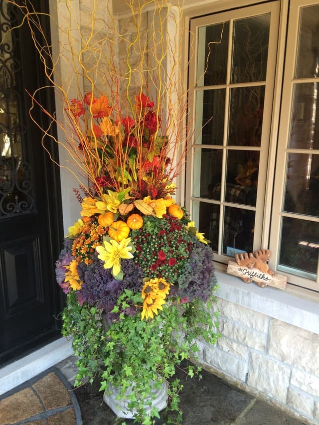 Fall planter of mums, kale, and curly willow branches by a front window