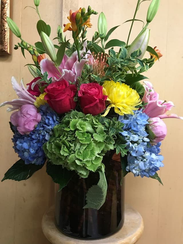 Bright fresh arrangement of roses, blue hydrangea, and lilies