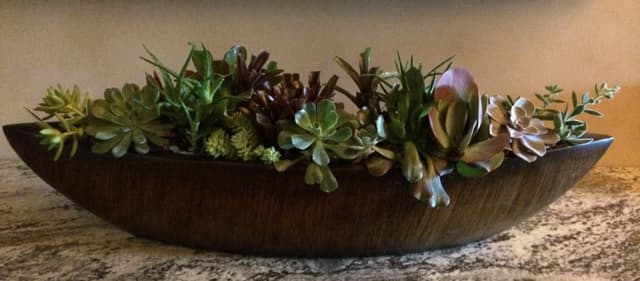Centerpiece of coral roses, succulents, and purple stock in a bronze bowl