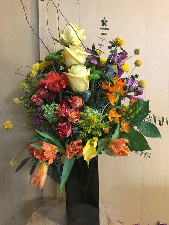 High-style arrangement in warm sunset tones with roses, calla lilies, and billy balls