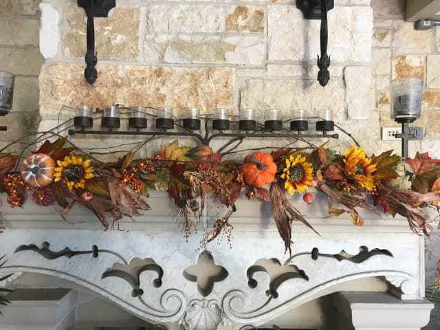 Outdoor stone mantel styled with fall garland, sunflowers, and candles