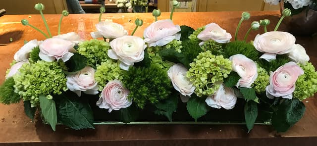 Soft centerpiece of white ranunculus, pink roses, and green viburnum