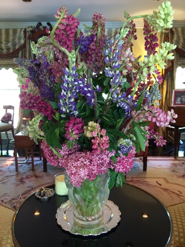 Tall luncheon arrangement of purple larkspur, roses, and spring flowers